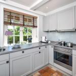 Küche mit hellen Schränken, Arbeitsplatte und Fenster mit Holzjalousie.