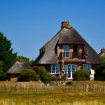 Haus mit Strohdach, Balkon und Garten. Umgeben von Bäumen und Gras.