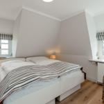 Bedroom with double bed, two windows, and wicker chair.