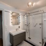 Bathroom with shower, sink, and mirror. Corridor to bedroom.