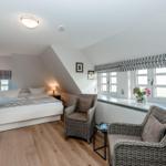 Bedroom with sloped ceiling, bed, two chairs, and windows with roller blinds.