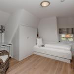 Bedroom with sloped ceiling, bed, wardrobe, and windows with blinds.