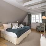 Schlafzimmer mit Doppelbett, zwei Sesseln und Fenster mit Vorhängen.