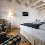 Schlafzimmer mit Bett, Sessel und Fernseher an der Wand.