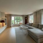 Wohnzimmer mit Sofa, Couchtisch und TV-Wand. Große Fenster und helle Holzböden.