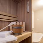 Sauna mit Holzbank, Eimer und Handtuch. Nebenraum mit Badewanne.