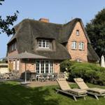 Dorfhaus mit Strohdach, Terrasse und Gartenliegen.