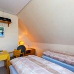 Zimmer mit zwei Betten, Fernseher und Schreibtisch unter schrägem Dach.