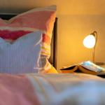 Bettkopf mit Kissen und Nachttisch mit Lampe und Buch.