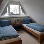 Zwei Einzelbetten mit blauen Bettwäschen unter einem Dachfenster.