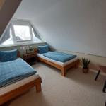 Zwei Einzelbetten mit blauen Bettwäsche unter einem Dachfenster.