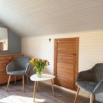 Zimmer mit zwei Stühlen, Tisch und Blumen. Holzwand und Dachschräge.