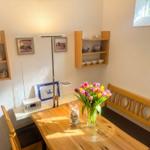 Holztisch mit Blumen, Sitzbank und Wandregale mit Tassen.
