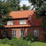 Rotes Ziegelhaus mit Dach und Fenstern, umgeben von Bäumen und Grün.