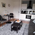 Wohnküche mit Sofa, Esstisch und Kochfeld. Teppich und Möbel sind schlicht.