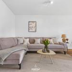 Ein Wohnzimmer mit einem hellen Sofa, einem runden Tisch und einem Beistelltisch.