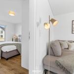 Wohnzimmer mit Sofa und Stehlampe. Nebenraum mit Bett und Fensterblick.