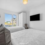 Zwei Betten mit weißen Bezügen, Fernseher und Fenster mit Blick auf Außenbereich.