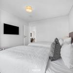Zwei Betten mit weißen Bettwäsche und Kissen. Wandfernseher und Holzregal an der Wand.