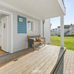 Haus mit Terrasse, Holzbank und Blick auf Grünfläche. Eingang führt in Wohnraum mit Sofa.