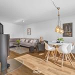 Wohn- und Essbereich mit Holzboden, Sofa, Esstisch und Kaminofen.