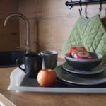 Küchenbereich mit Spüle, Tassen, Teller und Apfel auf Arbeitsplatte.