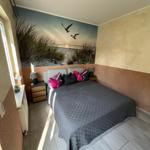 Schlafzimmer mit Bett, Nachttischen und Wandbild mit Strandmotiv.