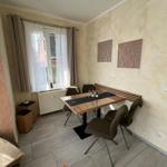 Esszimmer mit Tisch, Stühlen und Fenster. Wanddekoration und Bodenfliesen sichtbar.