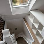 Treppenhaus mit Bücherregal und Dachfenster. Holzfußboden und weiße Wände.