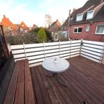 Terrasse mit Holzboden, Tisch und Bank. Blick auf Nachbarhäuser und Bäume.