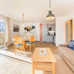 Wohn- und Essbereich mit Küche und Balkon. Möbel aus Holz und Sofa mit Kissen.
