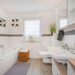 Badezimmer mit Badewanne, Waschbecken und Toilette. Dekorative Elemente wie Rettungsring und Pflanze.