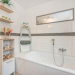 Badezimmer mit Badewanne, Spiegel und Holzregalen. Wandverkleidung mit dunkler Zierleiste.