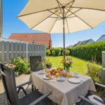 Terrasse mit Tisch, Stühlen und Sonnenschirm. Garten mit Blumen und Rasen.
