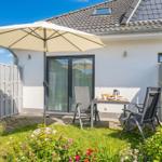 Terrasse mit Tisch, Stühlen und Sonnenschirm. Hintergrund: Haus mit Glastür und Zaun.