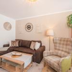 Wohnzimmer mit Sofa, Sessel und Tisch. Wanddekoration und Beleuchtung sichtbar.
