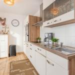 Küche mit Holz- und weißen Schränken, Spüle, Kaffeemaschine und Wanduhr.