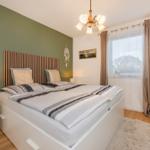 Schlafzimmer mit Doppelbett, grüner Wand und Fenster mit Vorhängen.