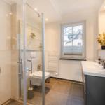 Badezimmer mit Dusche, Toilette und Waschbecken. Fenster mit Blick auf Haus.