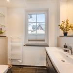Badezimmer mit Waschbecken, Toilette und Fenster. Pflanzen auf der Fensterbank.