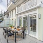 Terrasse mit Tisch und Stühlen, Glasfront und Balkon. Hinterhof mit Holzzaun.