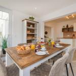 Essbereich mit Holztisch, Stühlen und Obstfrüchten. Küche im Hintergrund.