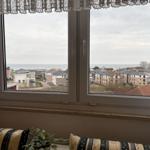 Durch das Fenster blickt man auf das Meer und Wohnhäuser.