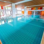 Großes Hallenbad mit blauem Wasser und Holzdecke.