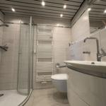 Bad mit Dusche, Waschbecken und Toilette. Weiße Fliesen und moderne Ausstattung.