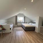Schlafzimmer mit Dachschräge, Bett, kleiner Schlafcouch und Fernseher.