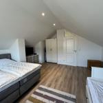 Schlafzimmer mit Doppelbett, Kinderbett und Holzboden unter schrägen Dachschrägen.