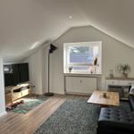 Wohnzimmer mit schwarzem Sofa, Holztisch und Fernseher unter schrägen Dachdecken.