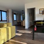 Wohnzimmer mit gelbem Sofa und Tischfußball. Holzboden und große Fenster.