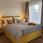 Schlafzimmer mit gelbem Bett, grauer Decke und Holzboden. An den Wänden hängen Vorhänge.